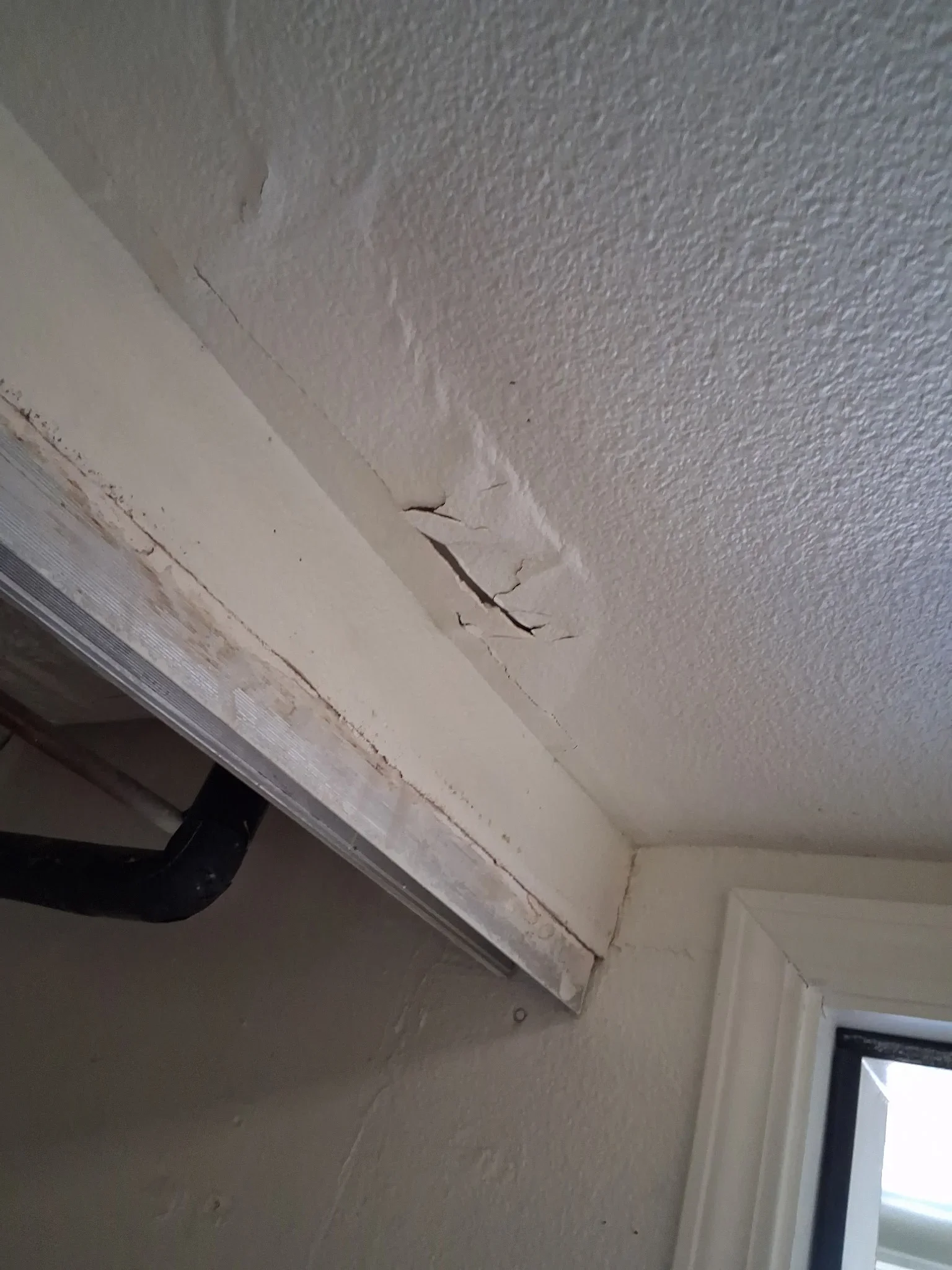 Cracked drywall ceiling with water staining and damage near soffit and window frame
