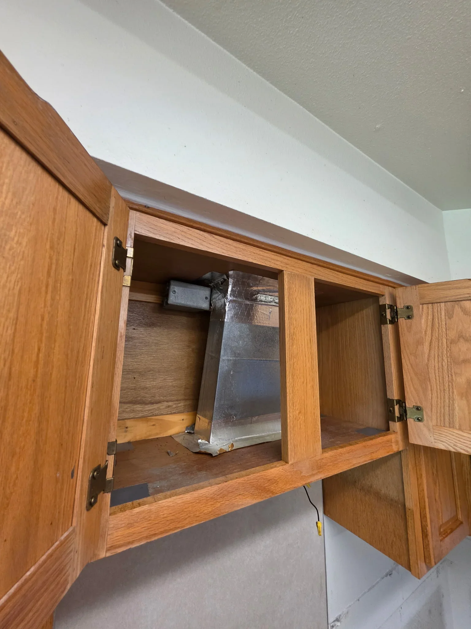 Open oak cabinet with copper plumbing lines and shut-off valve installed inside
