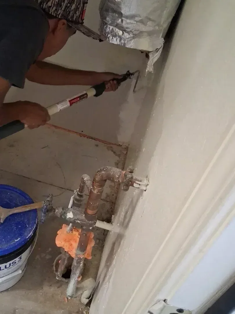 Worker applying joint compound to drywall patch with putty knife and brush
