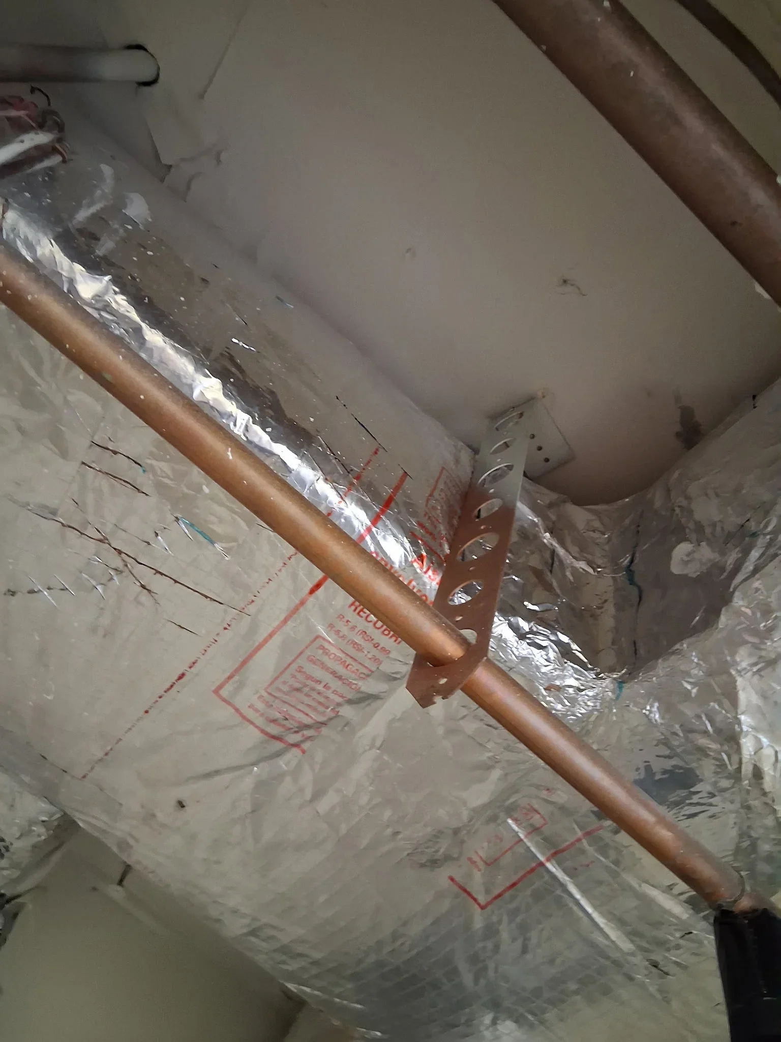 Copper water pipe with foam insulation and reflective vapor barrier, secured with metal bracket