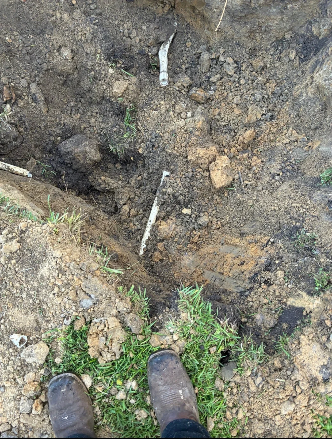 Underground trench showing white PVC utility pipe in excavated soil with grass and rocks